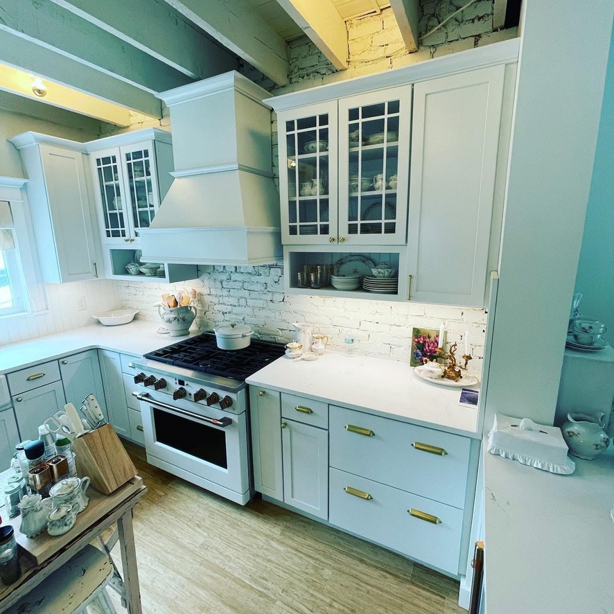Custom kitchen with soft blue cabinetry, white range hood and exposed brick backsplash